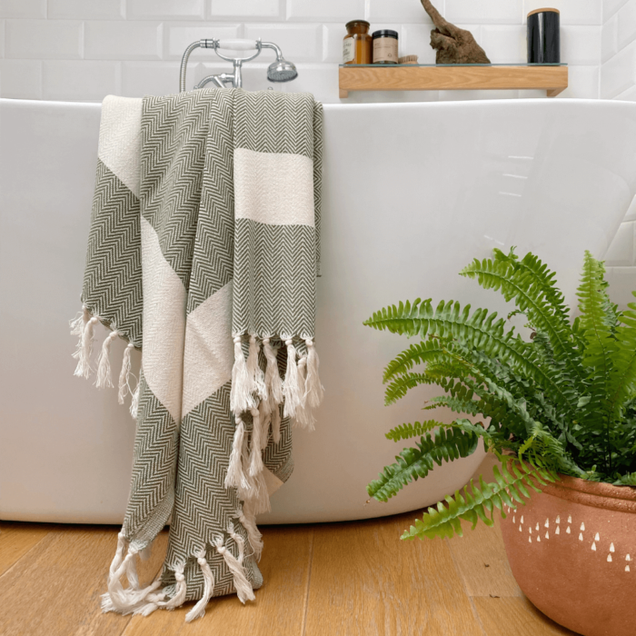 The Ferah organic cotton towel is a classic herringbone weave peshtemal with ecru block stripe & hand knotted tassels. Use it as a lightweight and quick drying towel, scarf, throw or sarong! 100 x 180 cm Seen here in moss green.