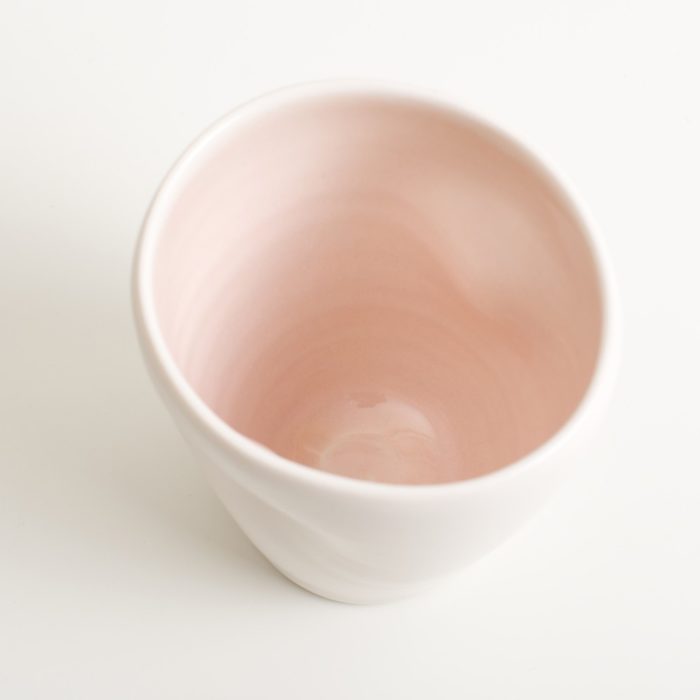 Handmade Dimpled Cup Pink Glaze. With a matt white glaze on the outside and soft coloured inside. Available in pale blue, pale pink, grey and turquoise. Perfectly formed dimples to fit in your hand, where the shape is inspired by Japanese tea traditions. Handmade by Linda Bloomfield in London. Sold on chalkandmoss.com.