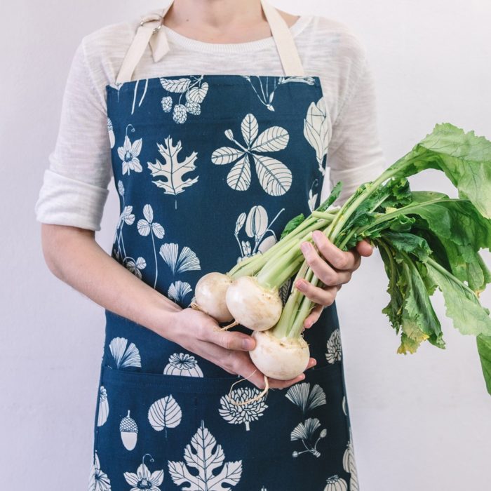 Botanical apron made from undyed cotton, and using water based dyes in the screen print. Available in several colours, seen here in indigo blue. By Softer + Wild, available on nature connected homeware shop Chalk & Moss.