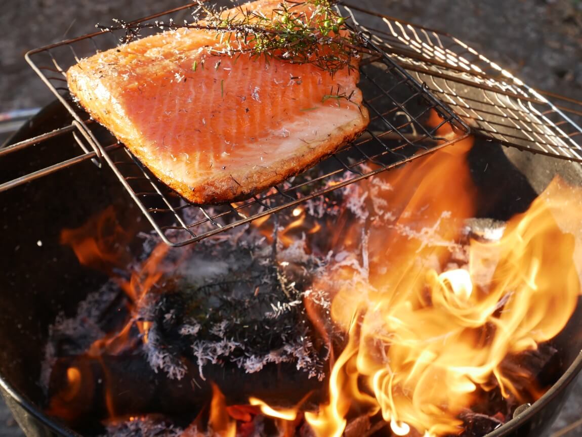 The juniper hot smoked salmon is nearly ready! See how it's crisped at the bottom of the salmon fillet and still wobbly on top? Perfect! In this recipe from Food from the Fire, you don't wait for charcoal but cook on the naked flame with juniper bushes for an extra special smoky flavour.