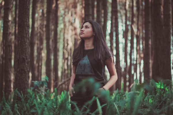 This woman is standing among the trees in the forest, looking up, contemplating, or perhaps looking at a bird. Spending time in nature does wonders for body and mind.