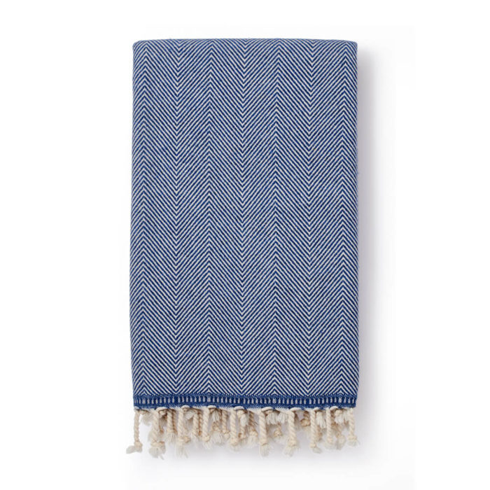 Wool throw made from an organic cotton and lambs wool blend, with a classic herringbone pattern. This makes it both warm and soft on the skin. 130 x 185cm. Seen here in denim (also available in grey).